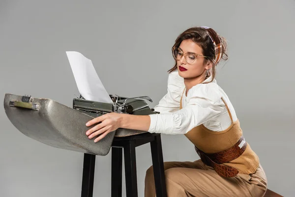 Стильная секретарша, открывающая корпус винтажной пишущей машинки, изолированной на сером — стоковое фото