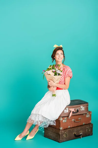 Счастливая женщина с цветами, сидящая на ретро-чемоданах на бирюзе — стоковое фото