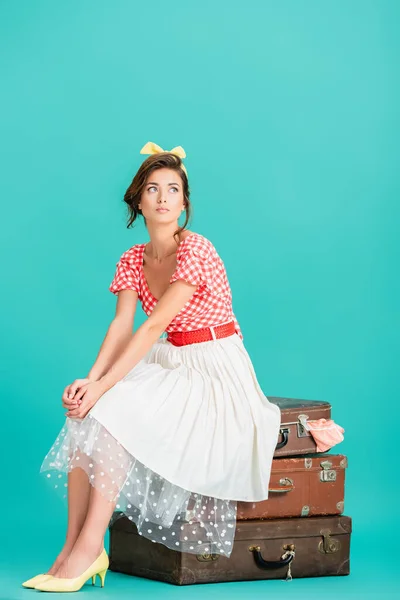 Pretty pin up woman sitting on vintage suitcases and looking away on turquoise — Stock Photo