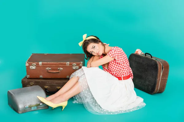 Souriant pin up femme regardant caméra près de valises vintage et machine à écrire au cas où sur turquoise — Photo de stock
