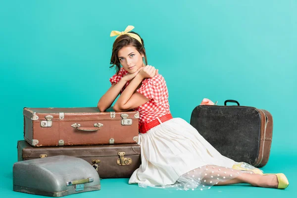 Smiling pin up woman looking at camera near suitcases and typewriter in case on turquoise — Stock Photo