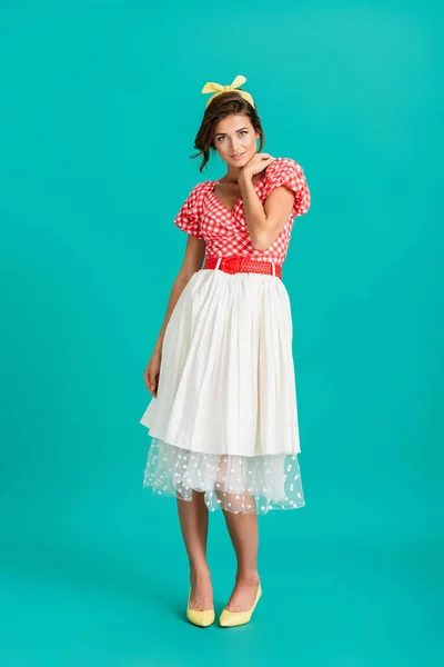 Full length view of young woman in retro clothes smiling at camera while posing on turquoise — Stock Photo