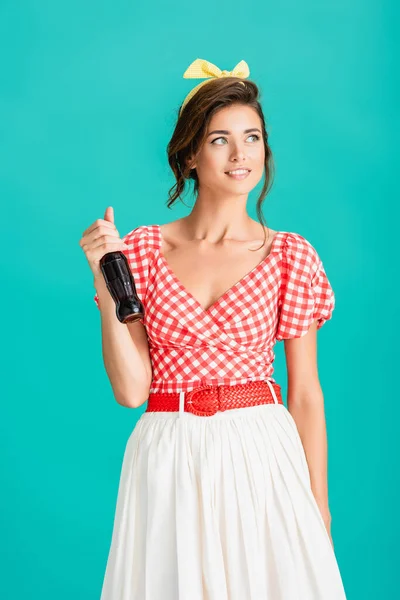 Sorridente pin up donna con bottiglia di soda distogliendo lo sguardo isolato sul turchese — Foto stock