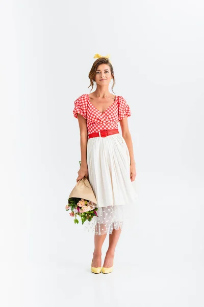 Full length view of young pin up woman holding bouquet while smiling at camera on white — Stock Photo
