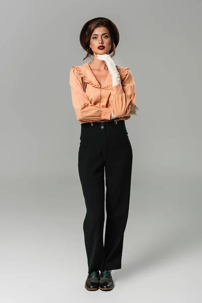 Young woman looking at camera while standing in fashionable retro clothes on grey — Stock Photo