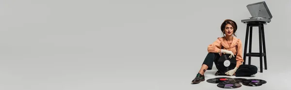 Модна жінка в вінтажному одязі, сидить на сірому біля вінілових дисків і рекордсменів, банер — стокове фото