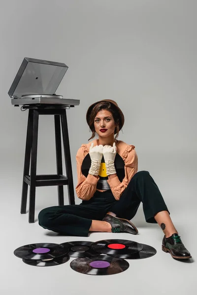 Красива жінка в модному ретро одязі, що сидить на підлозі біля вінілових дисків і записує гравця на сірому — стокове фото