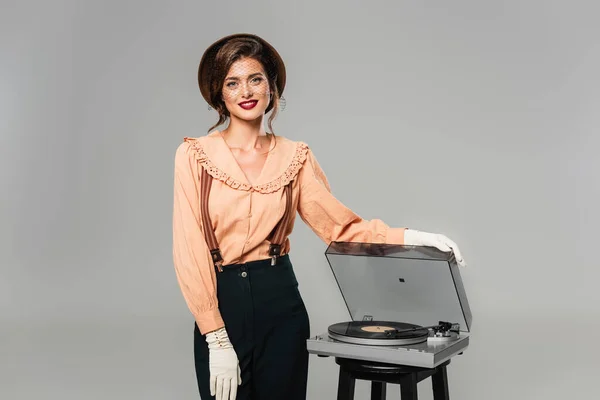 Happy woman in retro clothes smiling at camera while touching record player isolated on grey — Stock Photo