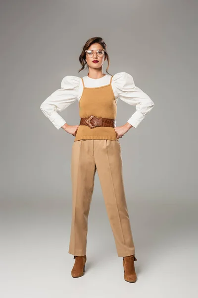 Vue pleine longueur de la jeune femme en vêtements rétro posant avec les mains sur les hanches sur le gris — Photo de stock