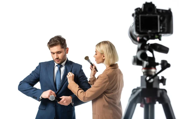 Blonde makeup artist with cosmetic brush near news anchor buttoning his blazer isolated on white, blurred foreground — Stock Photo