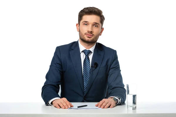 Nachrichtensprecher blickt in die Kamera, während er am Arbeitsplatz in der Nähe von Papieren sitzt und ein Glas Wasser isoliert auf weiß — Stockfoto