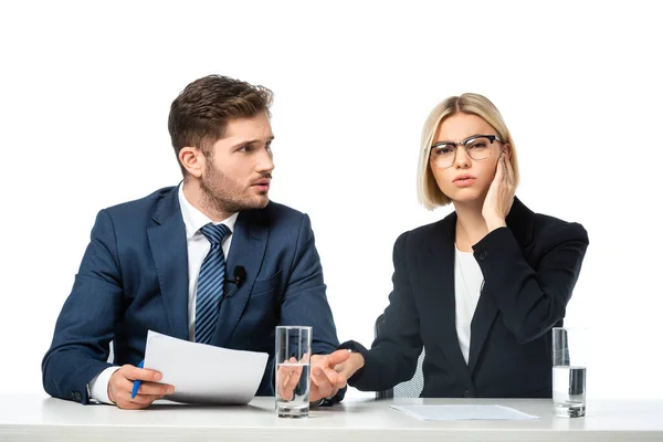 Serious blonde anchorwoman adjusting earphone near colleague isolated on white — Stock Photo