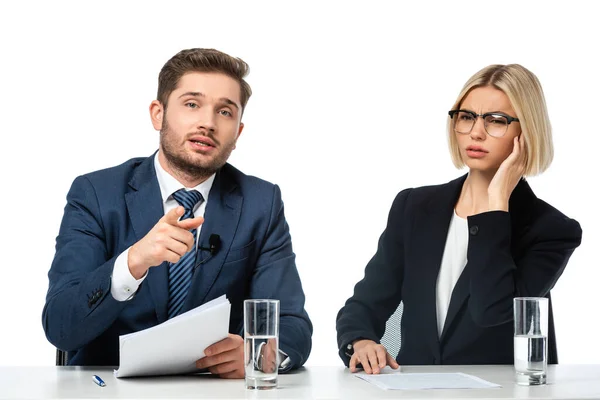 Anchorman pointing with finger at camera near colleague adjusting earphone isolated on white — Stock Photo