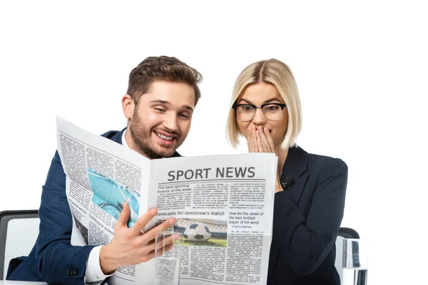 Sonriente presentador de noticias mostrando periódico a colega sorprendido aislado en blanco - foto de stock