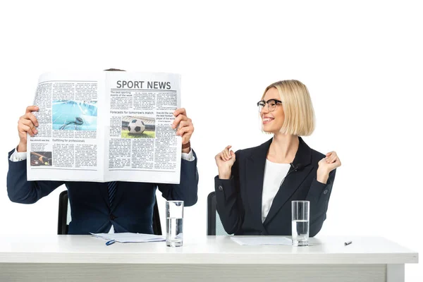 Fröhliche Moderatorin neben Kollegin verdeckt Gesicht mit Zeitung isoliert auf Weiß — Stockfoto