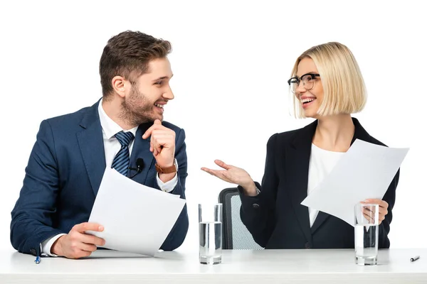 Cheerful anchorwoman pointing with hand at smiling colleague at workplace isolated on white — Stock Photo