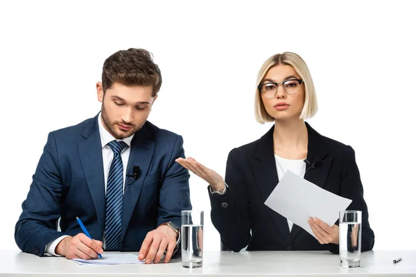 Young blonde broadcaster pointing at colleague writing at workplace isolated on white — Stock Photo