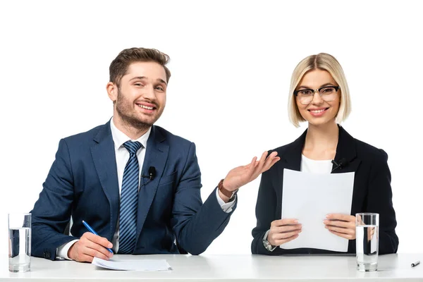 Happy news anchor pointing at smiling colleague holding paper at workplace isolated on white — Stock Photo