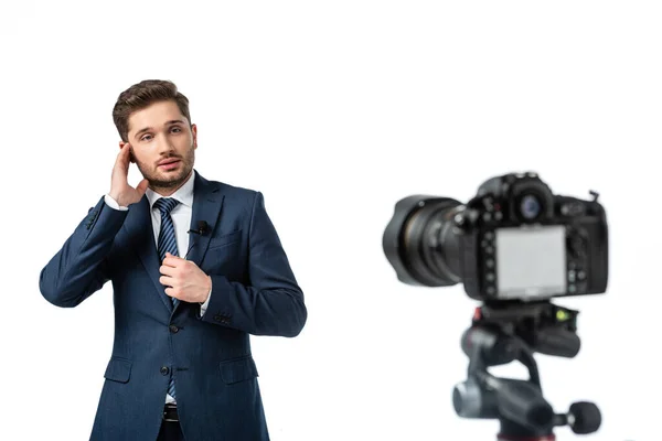 Jovem emissora ajustando fone de ouvido perto da câmera digital em primeiro plano desfocado isolado no branco — Fotografia de Stock