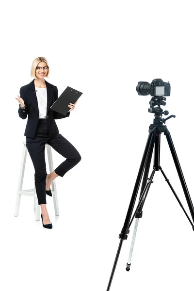 Full length view of smiling news anchor on high stool pointing with hand near digital camera on tripod — Stock Photo