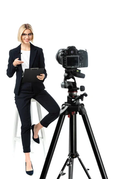 Smiling broadcaster pointing at clipboard near digital camera on white, blurred foreground — Stock Photo