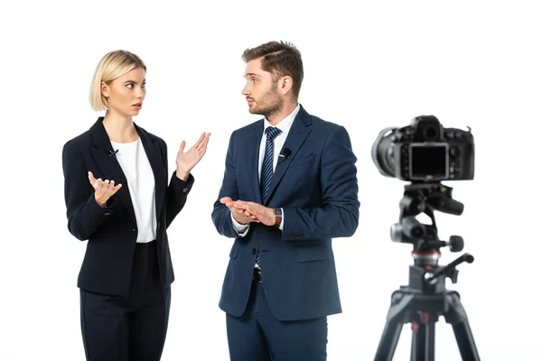 Emissora espantada gesticulando perto colega e câmera digital em primeiro plano desfocado isolado no branco — Fotografia de Stock