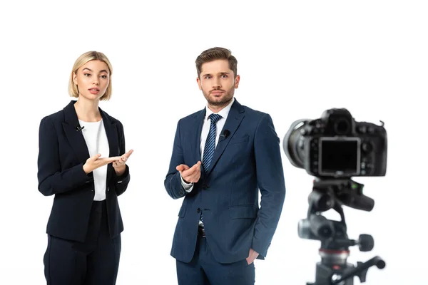 Couple of news anchors working near digital camera on blurred foreground isolated on white — Stock Photo