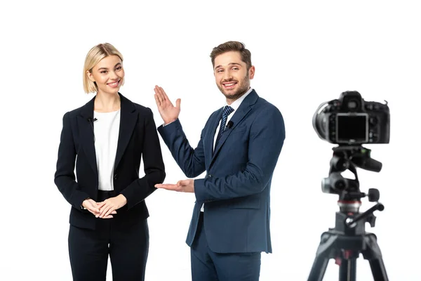 Happy news anchor pointing at colleague near digital camera on blurred foreground isolated on white — Stock Photo