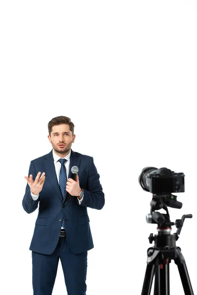 Nachrichtenkommentator mit Mikrofon gestikulierend, während er in der Nähe der Digitalkamera auf unscharfem, weiß isoliertem Vordergrund spricht — Stockfoto