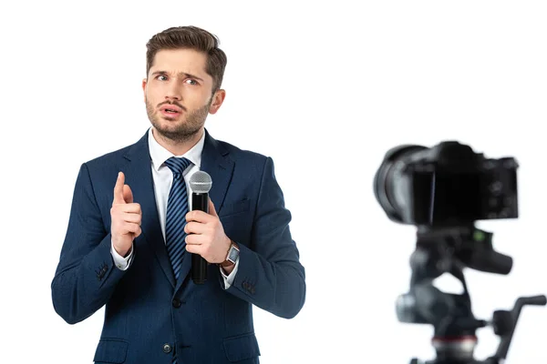 Seriöse Nachrichtenmoderatorin mit Mikrofon, das mit dem Finger in der Nähe der Digitalkamera auf unscharfem, auf weiß isoliertem Vordergrund zeigt — Stockfoto