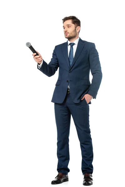 Vista completa del ancla de noticias sosteniendo la mano en el bolsillo mientras está de pie con micrófono en blanco - foto de stock