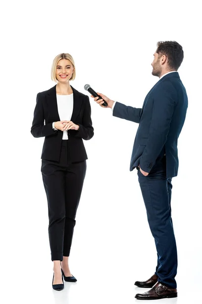 Ansicht des Moderators in voller Länge mit der Hand in der Tasche, der ein Interview mit einer lächelnden Geschäftsfrau auf Weiß führt — Stockfoto