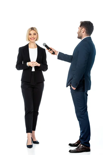 Full length view of anchorman with hand in pocket taking interview from smiling businesswoman on white — Stock Photo