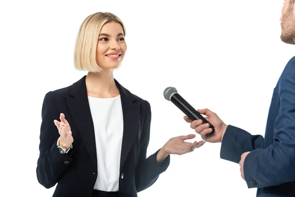 Lächelnde blonde Geschäftsfrau spricht in der Nähe von Interviewer mit Mikrofon isoliert auf weiß — Stockfoto