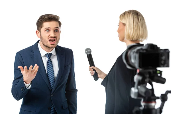 Periodista rubia entrevistando hombre de negocios enojado cerca de la cámara digital en primer plano borroso aislado en blanco - foto de stock