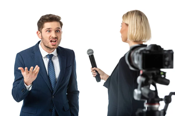 Blondine Journalistin interviewt wütenden Geschäftsmann in der Nähe Digitalkamera auf verschwommenem Vordergrund isoliert auf weiß — Stockfoto