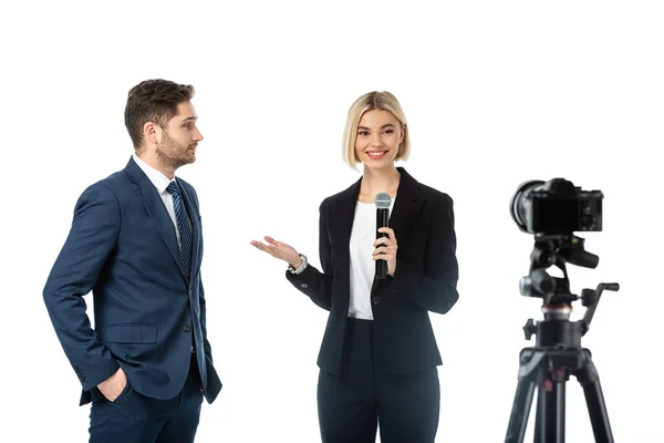 Sonriente presentador de noticias con micrófono apuntando al hombre de negocios cerca de la cámara digital aislado en blanco, borrosa primer plano - foto de stock