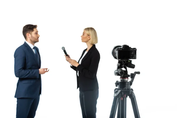 Side view of businessman talking during interview with blonde anchorwoman isolated on white, blurred foreground — Stock Photo