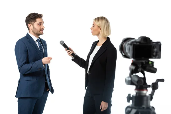 Junger Geschäftsmann gibt blonder Journalistin Interview mit Mikrofon in der Nähe von Digitalkamera auf unscharfem Vordergrund isoliert auf Weiß — Stockfoto