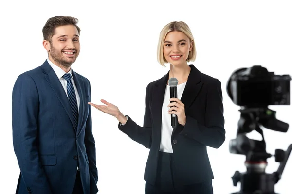 Présentateur de nouvelles souriant pointant vers homme d'affaires heureux lors d'une interview près de l'appareil photo numérique isolé sur blanc, au premier plan flou — Photo de stock