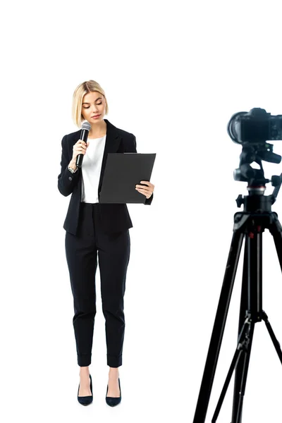Blonde Nachrichtensprecherin im schwarzen Anzug in der Nähe der Digitalkamera in voller Länge auf weißem, verschwommenem Vordergrund — Stockfoto