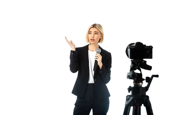 Triste presentadora con micrófono apuntando con la mano cerca de la cámara digital en primer plano borroso aislado en blanco - foto de stock