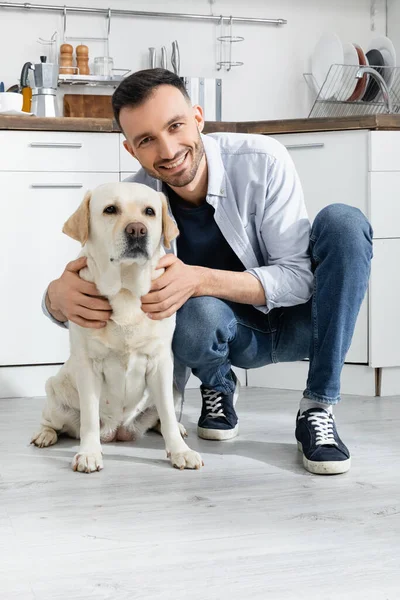 Allegro uomo in jeans seduto e coccole labrador a casa — Foto stock