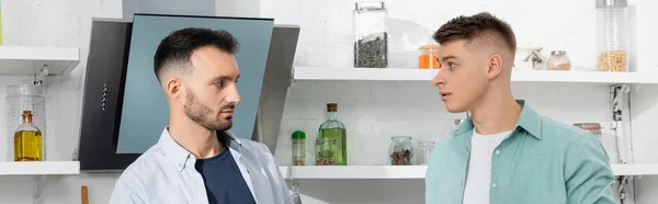 Confused homosexual men looking at each other in kitchen, banner — Stock Photo