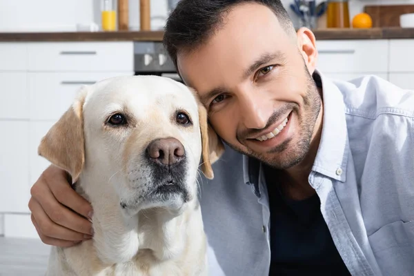 Cheerful bearded man smiling near labrador at home — Stock Photo