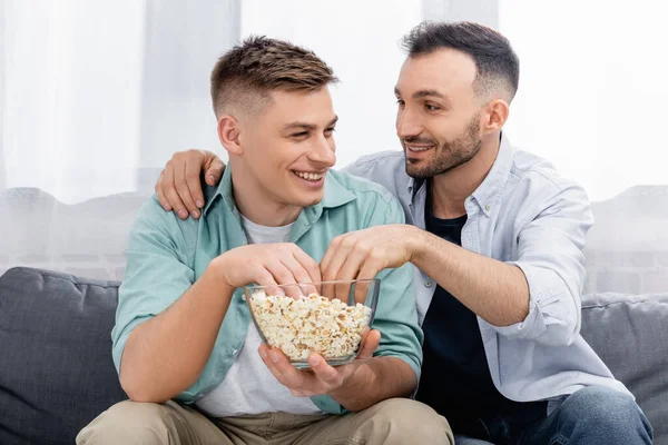 Cheerful same sex couple looking at each other while reaching popcorn — Stock Photo