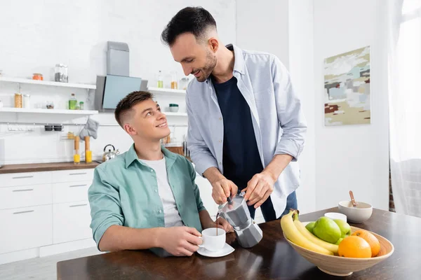 Homem homossexual feliz derramando café perto do marido na cozinha — Fotografia de Stock
