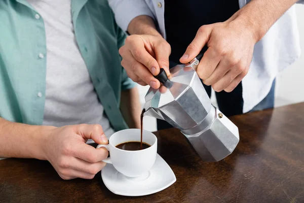 Обрізаний вид гомосексуального чоловіка наливає каву в чашку біля чоловіка — стокове фото