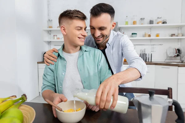 Felice uomo omosessuale versando latte in ciotola con fiocchi di mais — Foto stock