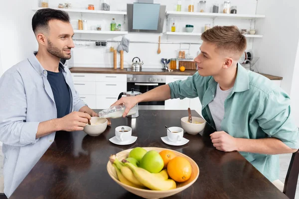 Uomo omosessuale versando latte in ciotola con fiocchi di mais vicino marito — Foto stock